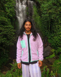 Man wearing a cozy lavender fleece jacket with mint green accents, standing in front of a lush waterfall background.