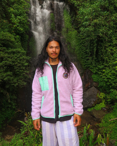 Man wearing a cozy lavender fleece jacket with mint green accents, standing in front of a lush waterfall background.