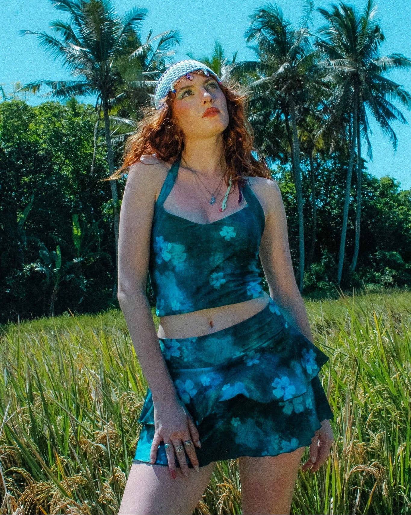 Woman in a blue green floral skirt standing in a field with palm trees in the background
