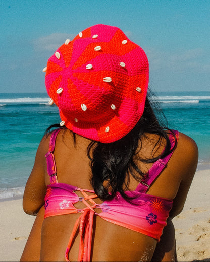 Person wearing a bright pink and red sun hat on a beach with ocean view